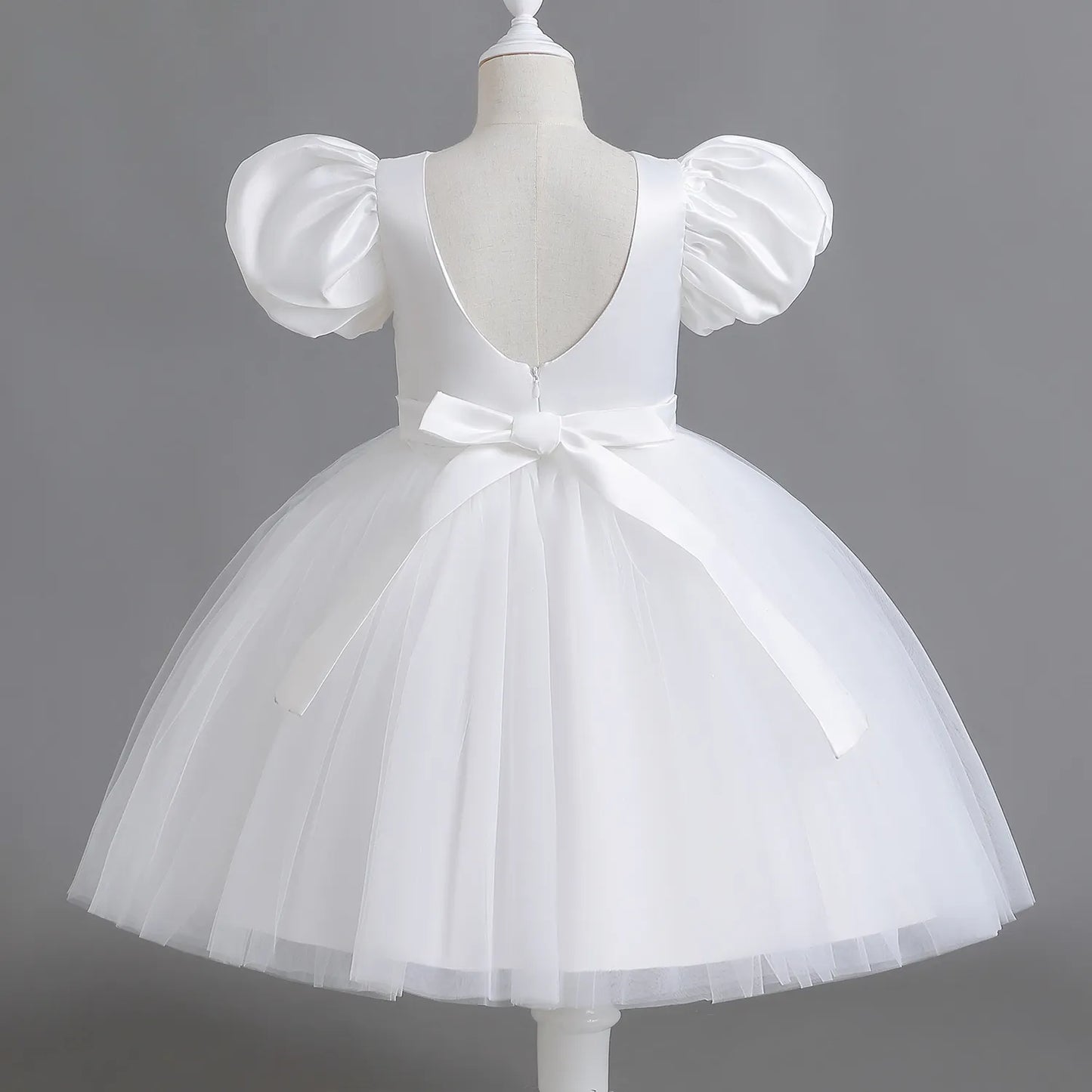 Introducing the "Timeless Elegance" Flower Girl Dress in White – a captivating blend of sophistication and playfulness. With puff sleeves, a U-shaped open back, and a large bow, this dress creates a magical silhouette. The silk-like top ensures comfort, while the very puffy tulle skirt adds a whimsical touch. Perfect for capturing cherished moments on your special day. Make dreams come true – order now for an enchanting celebration!